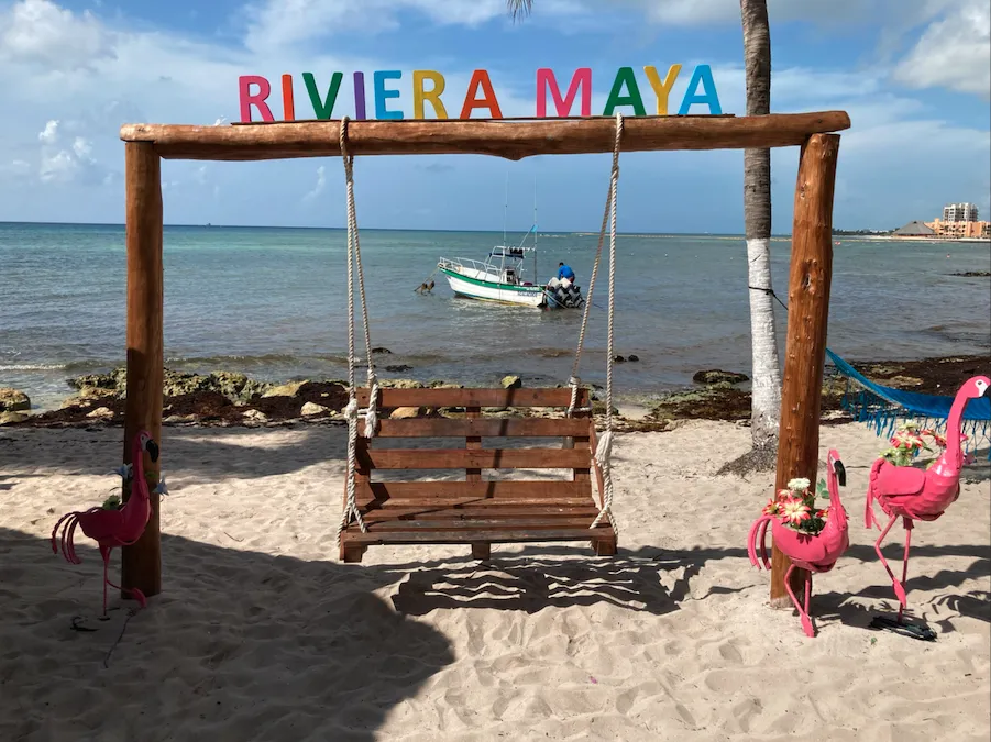Balançoire en bois sur la plage sous l’enseigne colorée Riviera Maya, avec des flamants roses décoratifs